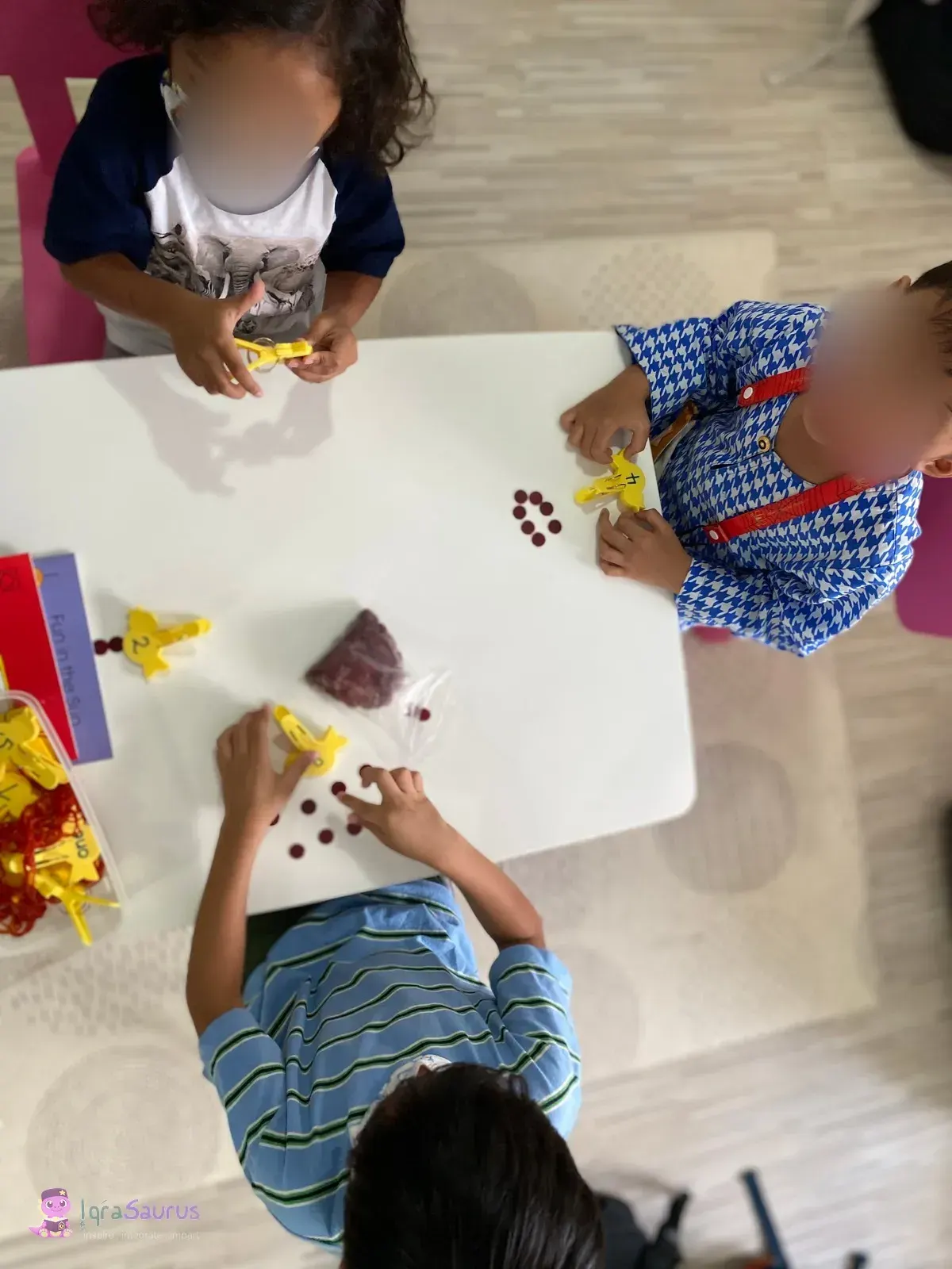 Three children at a small white table counting red counters against yellow number pegs