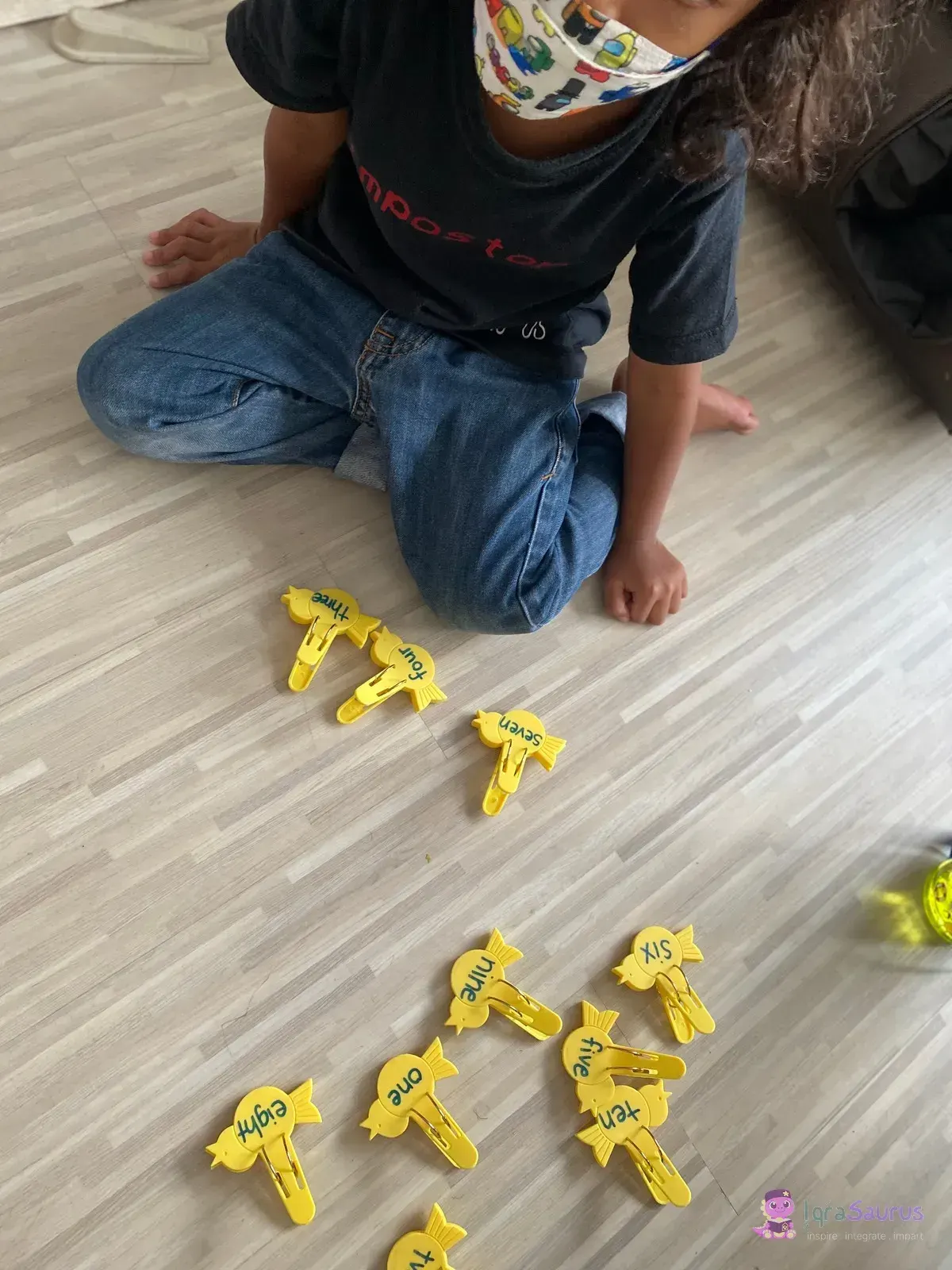 A child kneeling on the floor beside yellow pegs printed with the number words one to ten