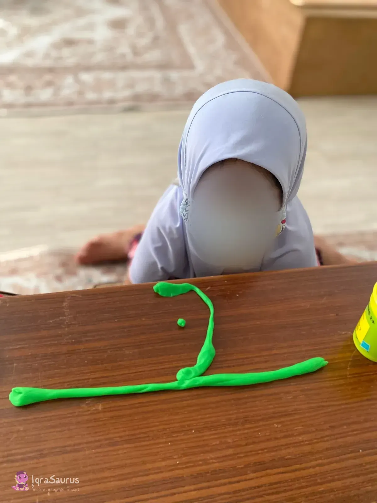 Green plasticine rolled and shaped into a letter on a wooden table