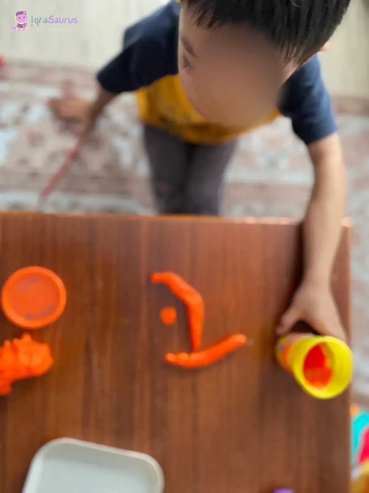 A boy shaping orange plasticine into a letter, with tubs of plasticine beside him