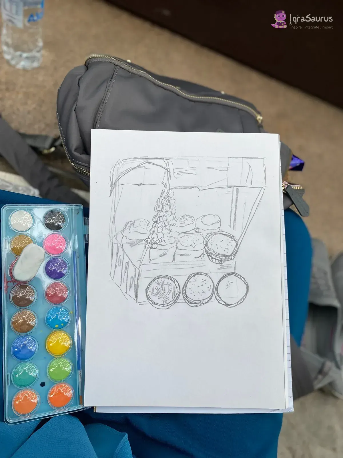 A pencil drawing of a stall on a clipboard, next to an open watercolour palette