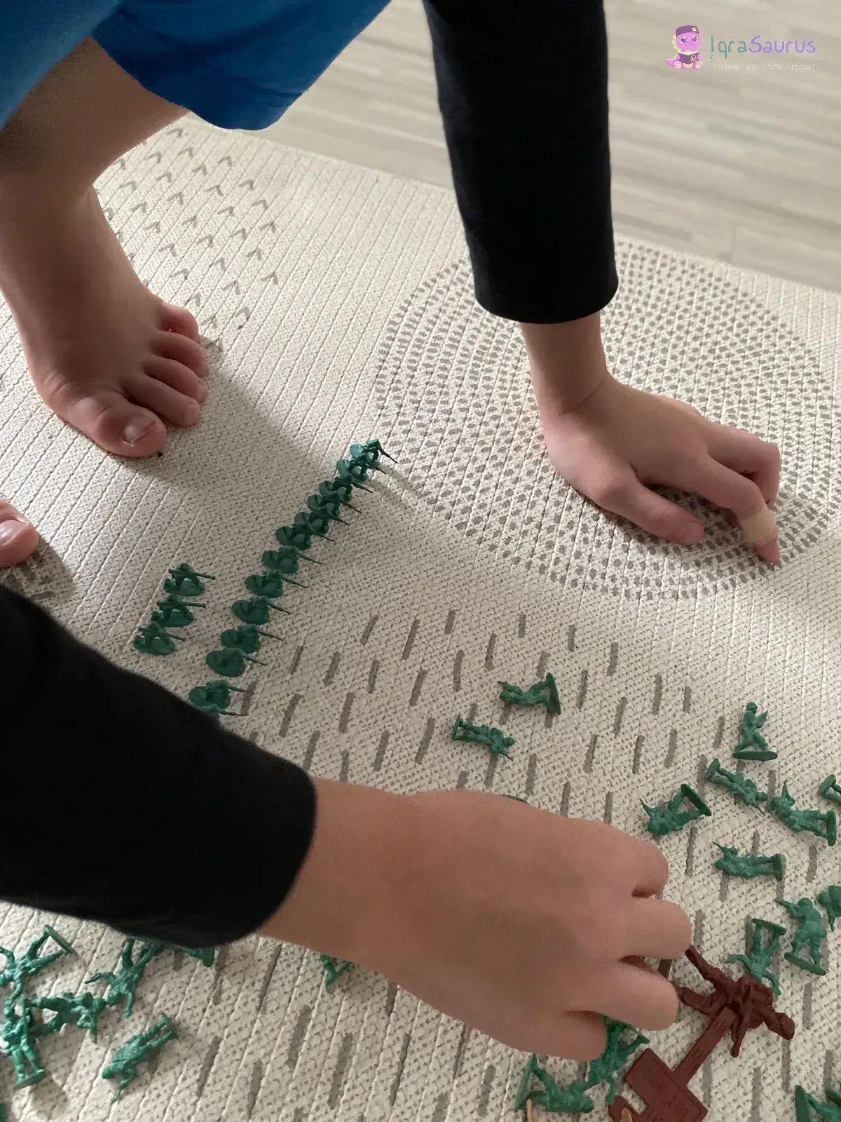 Children's hands lining up small green toy soldiers on a mat